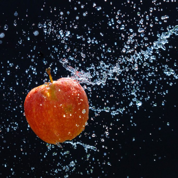 Rote Apfel, umgeben von spritzendem Wasser vor schwarzem Hintergrund.