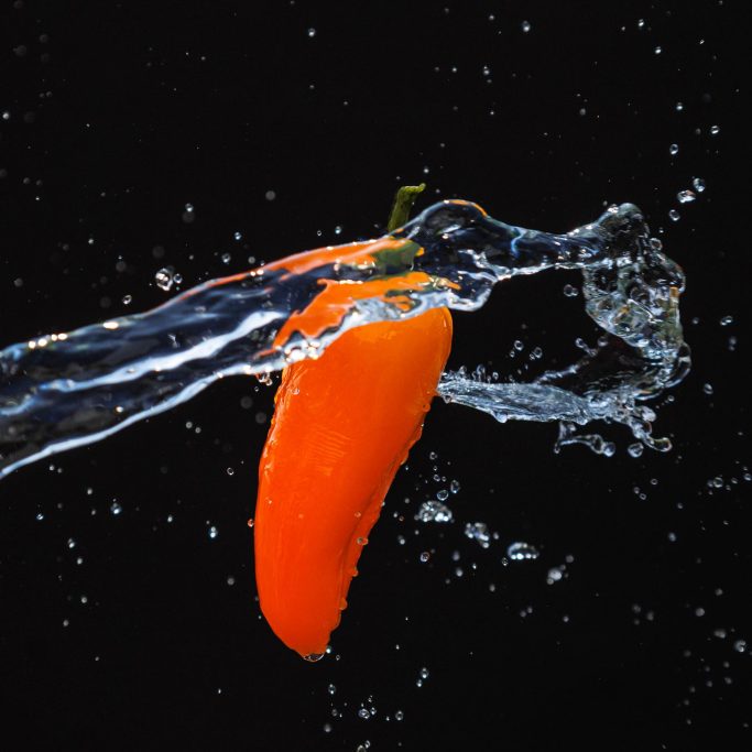 Eine orange Karotte wird von Wasser umgeben, auf schwarzem Hintergrund.