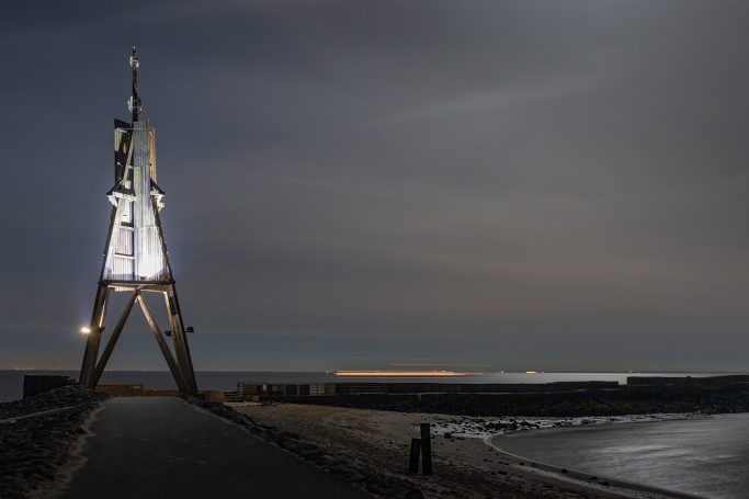 Leuchtturm an der Küste bei Nacht, umgeben von sanften Wellen und Wolken.