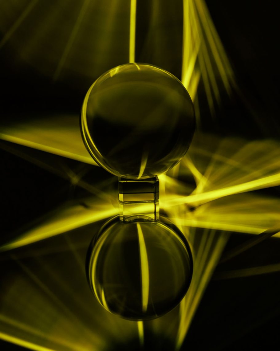 Kugel mit reflektierender Oberfläche vor gelbem, strahlendem Hintergrund.