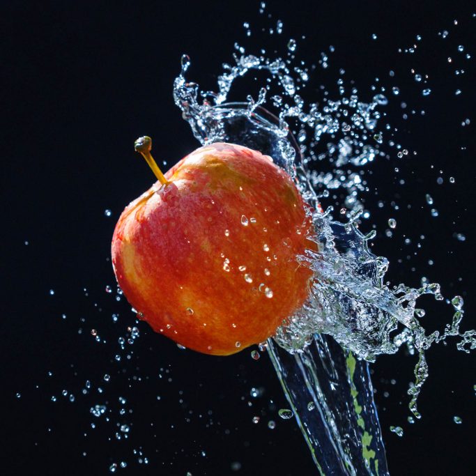 Rote Apfel, der von Wasser umgeben ist, spritzt und erzeugt sprudelnde Wassertropfen.