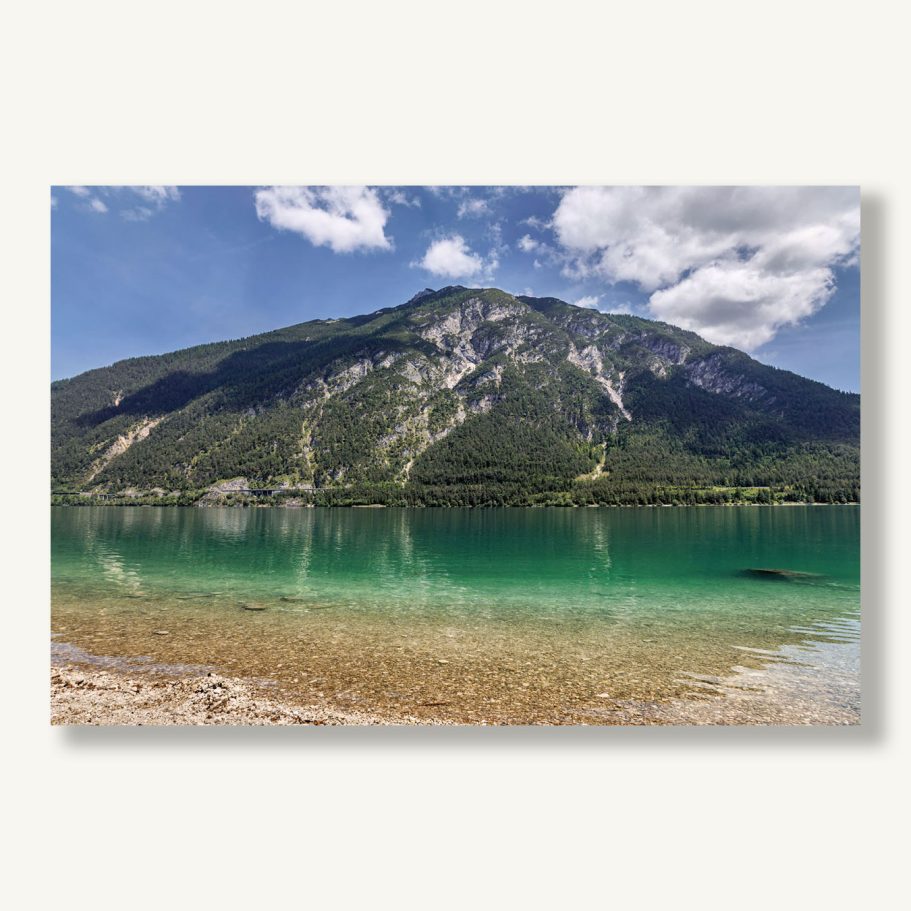 Ein klarer See mit grünerem Wasser und einem bewaldeten Berg im Hintergrund.