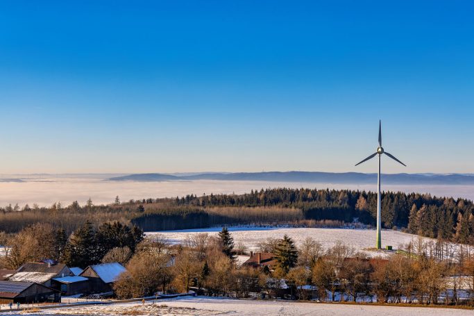 Landschaft mit Windrad, schneebedeckten Feldern und weitem, klarem Himmel.