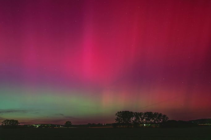 Leuchtendes Polarlicht in pinken und grünen Tönen über einer Landschaft.