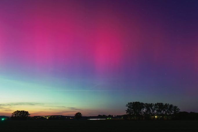 Bunte Aurora mit lila und pinken Streifen am Nachthimmel über einer Landschaft.