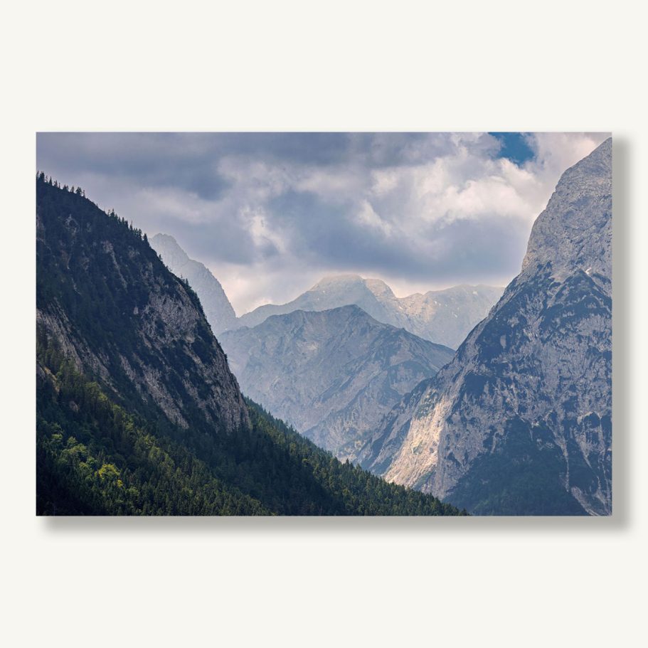 Berglandschaft mit hohen Gipfeln und bewaldeten Tälern unter bewölktem Himmel.