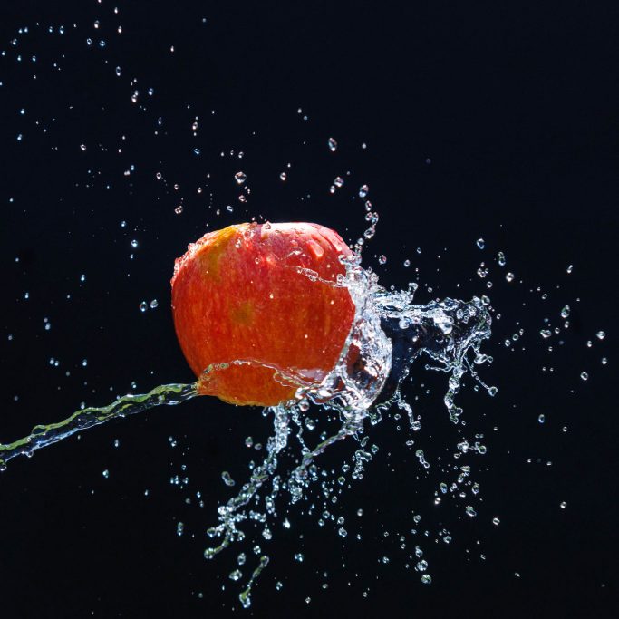 Rote Apfel spritzt Wasser vor einem dunklen Hintergrund.