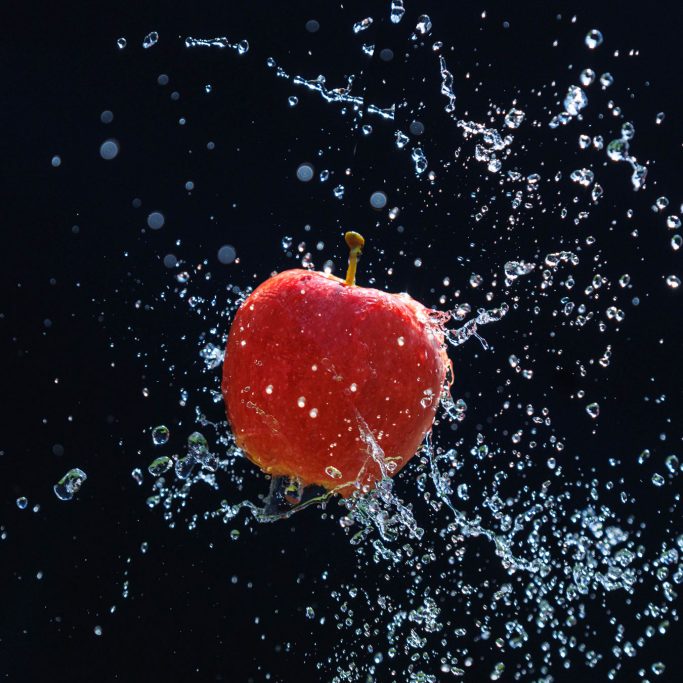 Rote Apfel spritzt Wasser auf einem dunklen Hintergrund.