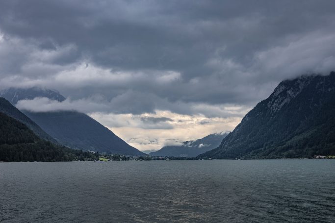 Blick auf einen See, umgeben von Bergen unter einem bewölkten Himmel.