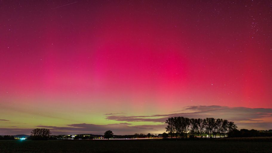Nordlichter in pink und grün über einem ländlichen Horizont bei Dämmerung.