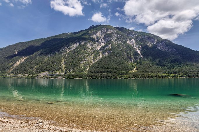Berglandschaft mit grünem Wasser und klarem Himmel, reflektiert im See.