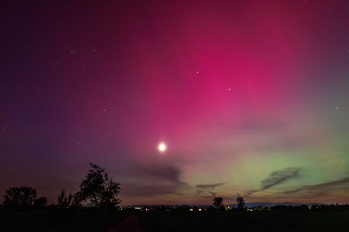 Farbige Polarlichter am Nachthimmel mit Mond und Wolken.