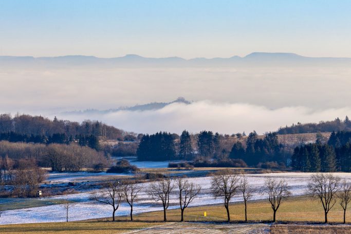 Berglandschaft mit Nebel und schneebedeckten Wiesen im Vordergrund.