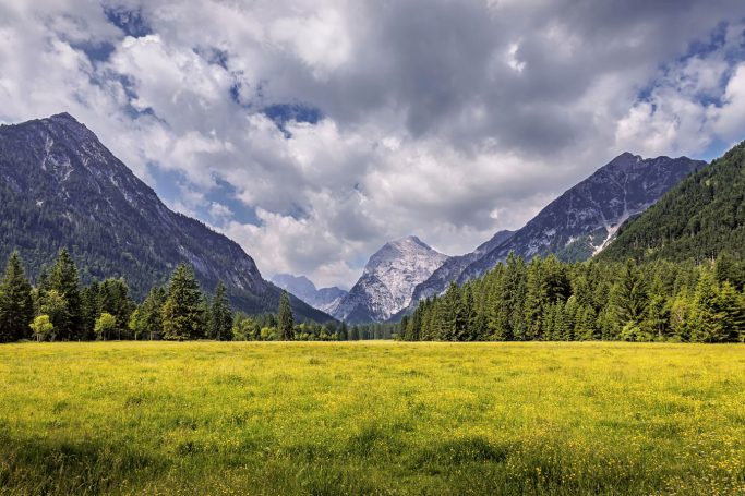 Grüne Wiese umgeben von Bergen und dramatischem Wolkenhimmel.